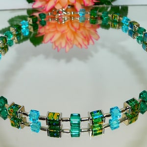 May include: A double-strand necklace made with square-shaped glass beads in shades of turquoise and green. The beads are separated by silver metal spacers.