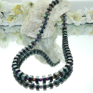 May include: A black necklace made of iridescent square-shaped beads. The necklace is layered and has a reflective surface.