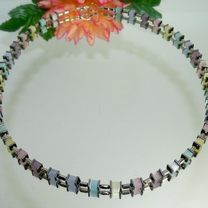 May include: A pastel colored necklace made of square beads with silver metal links. The necklace is made of a repeating pattern of pastel colored squares and silver metal links.