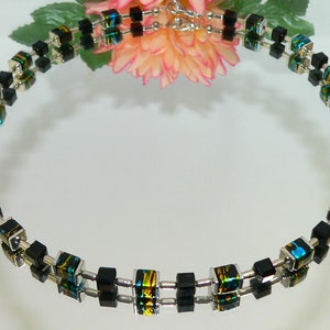 May include: A black and silver necklace with square beads. The beads have a green, blue, and gold iridescent finish.