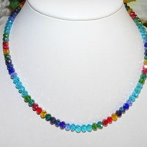 May include: A colorful beaded necklace displayed on a white mannequin. The necklace features a gradient of colors, including red, orange, yellow, green, blue, and purple. The beads are small and faceted, reflecting light.