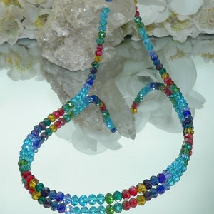 May include: A multi-strand necklace featuring a gradient of colorful beads. The beads transition from red to yellow, green, blue, and purple. The necklace has a silver clasp and is displayed on a reflective surface.