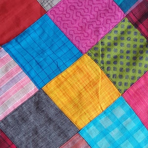 Könnte beinhalten: Ein Patchwork-Deckenstück aus verschiedenen Stoffen in den Farben Rot, Pink, Blau, Grün, Gelb und Grau. Die Stoffe sind in einem Rautenmuster zusammengenäht.