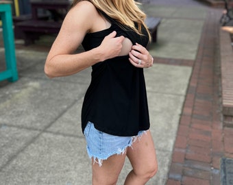 May include: A black sleeveless nursing tank top with a built-in nursing panel. The tank top is being worn by a person with blonde hair and is paired with denim shorts.