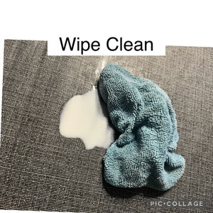 May include: A blue microfiber cleaning cloth on a gray textured surface with a white stain. The text "Wipe Clean" is above the cloth.