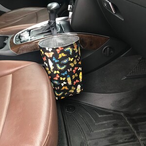 May include: A black fabric car trash can with a butterfly print hanging on the side of a car seat.