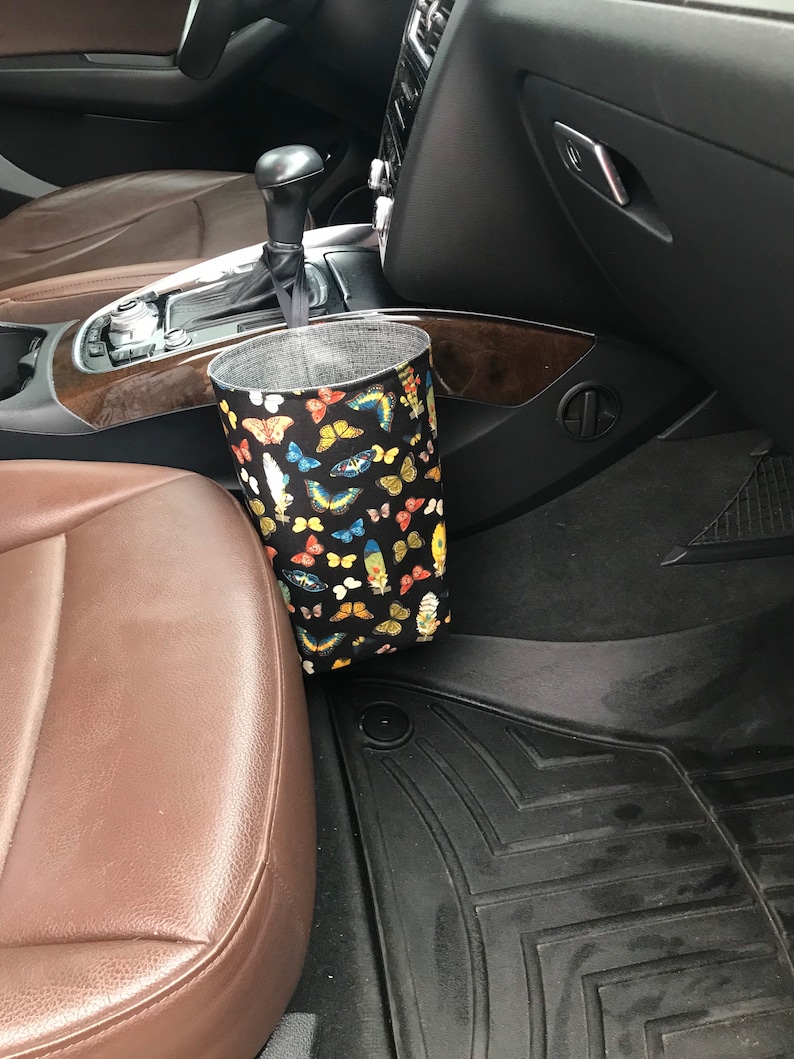 May include: A black fabric car trash can with a butterfly print hanging on the side of a car seat.