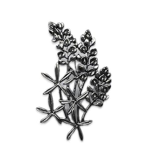 May include: Silver-toned brooch featuring a cluster of stylized bluebonnet flowers. The brooch is a detailed representation of the Texas state flower.