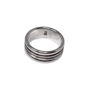May include: A silver ring with a triple-band design. The ring has a smooth, polished finish and a minimalist aesthetic. The inside of the ring is stamped with a small mark. This ring is a piece of jewelry.