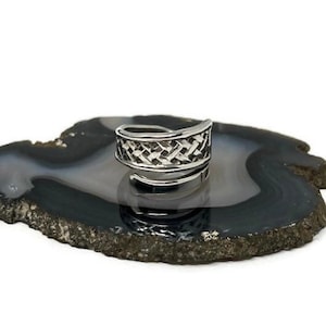 May include: A silver ring with a woven design. The ring is on a gray and black agate slice.