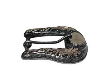 May include: A metal belt buckle featuring a dark, textured finish with raised, polished silver-tone floral engravings. The buckle has a curved, U-shaped frame and includes a central prong mechanism for securing a belt strap.