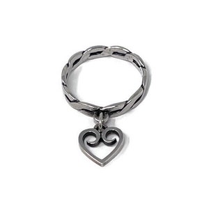 May include: A silver ring with a braided band and a dangling heart charm. The heart charm has a stylized design with two loops.