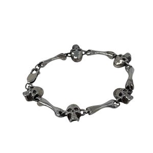 May include: A silver-toned bracelet featuring a series of skull and bone-shaped links. The bracelet has a lobster clasp closure. The design is detailed and gothic in style.