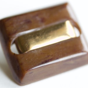 May include: A brown rectangular button with a gold metal insert. The button has a smooth, glossy finish.