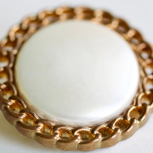 May include: A white button with a gold chain-link design around the edge.
