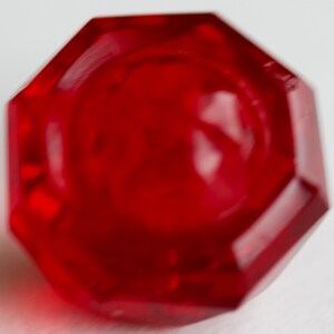 May include: A red octagonal glass knob with a smooth, shiny surface.