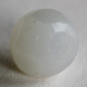 May include: A smooth, off-white, spherical object. The surface has subtle variations in tone and small, darker spots. The shape is rounded and appears to be a single, solid piece. The object is set against a soft, white background.