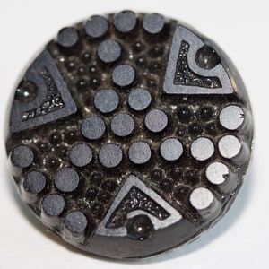 Puede incluir: Botón de vidrio negro con un diseño geométrico en relieve y una superficie texturizada.