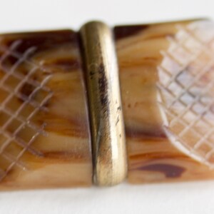 May include: A rectangular brown and white patterned button with a gold metal band in the center.