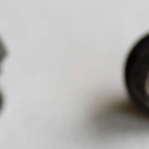 May include: Two black buttons with a silver shank. One button is round and the other is a more geometric shape.