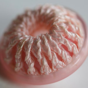 Könnte beinhalten: Ein rosa Knopf mit einem weißen Häkelmuster. Der Knopf hat ein Loch in der Mitte.