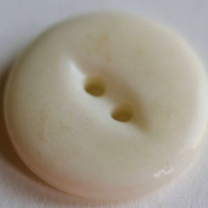 May include: A white plastic button with two holes. The button is slightly textured and has a slightly off-white color.