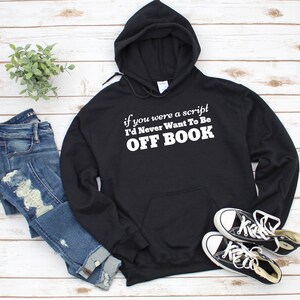 Op de afbeelding: Zwart hoodie met witte tekst die luidt: "Als je een script was, zou ik nooit off book willen zijn."