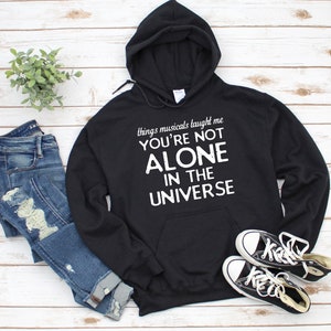 Może przedstawiać: Czarna bluza z kapturem z napisem "things musicals taught me you're not alone in the universe" w białym kolorze.