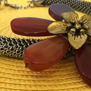 May include: A silver chain necklace with a flower pendant made of red carnelian stones and a gold-toned metal flower with a detailed design.