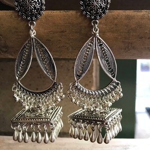 Puede incluir: Un par de pendientes de plata con intrincados dise&ntilde;os de filigrana. Los pendientes tienen una parte superior redonda con un patr&oacute;n floral y un colgante en forma de l&aacute;grima con una parte inferior cuadrada. Los pendientes est&aacute;n adornados con peque&ntilde;as cuentas de plata y colgantes en forma de l&aacute;grima.