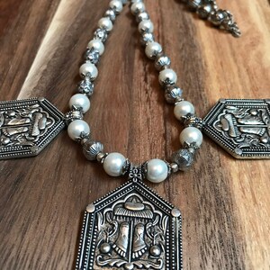 Puede incluir: Un collar de plata con cuentas de perlas blancas y tres colgantes de plata adornados. Los colgantes tienen forma de oct&oacute;gonos y presentan dise&ntilde;os intrincados.