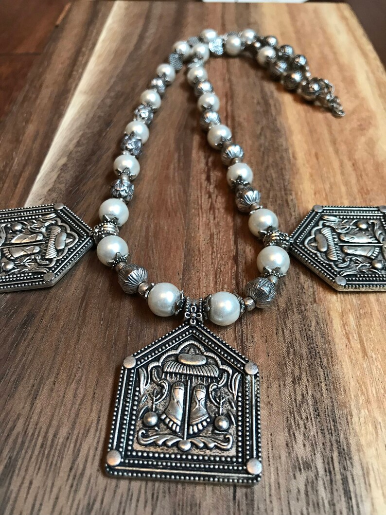 Puede incluir: Un collar de plata con cuentas de perlas blancas y tres colgantes de plata adornados. Los colgantes tienen forma de oct&oacute;gonos y presentan dise&ntilde;os intrincados.