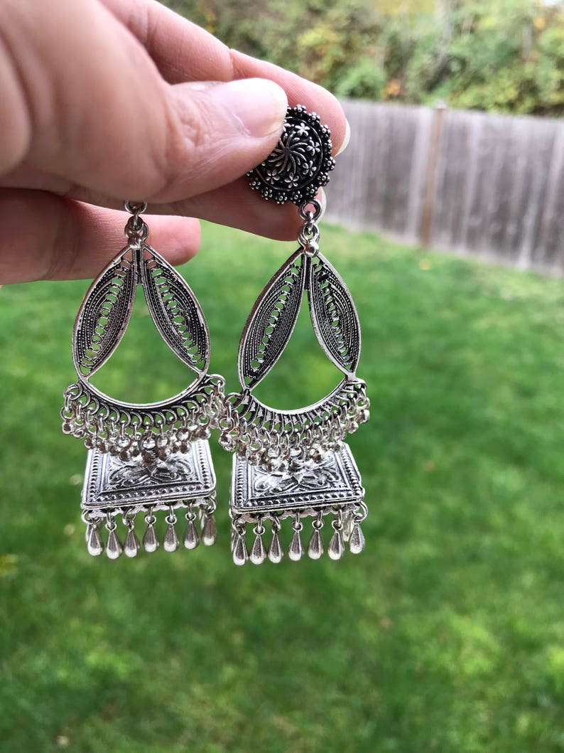 Puede incluir: Pendientes de plata con forma de l&aacute;grima y dise&ntilde;o cuadrado. Los pendientes tienen un dise&ntilde;o floral plateado y una borla plateada.