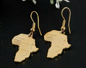 May include: A pair of gold-tone earrings featuring a map of Africa. The earrings are made of metal and have a dangling design.