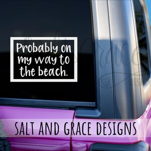 May include: A white vinyl decal with the text "Probably on my way to the beach" in a black rectangle. The decal is on a vehicle window. The bottom of the image shows the text "SALT AND GRACE DESIGNS".