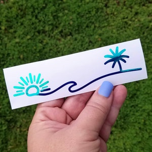 Puede incluir: Una pegatina con un dise&ntilde;o degradado azul y verde que presenta un sol, una ola y una palmera. La pegatina est&aacute; sobre un fondo blanco.