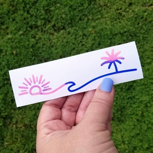Puede incluir: Una pegatina con un dise&ntilde;o de puesta de sol rosa y azul, una ola y una palmera. La pegatina est&aacute; sobre un fondo blanco.
