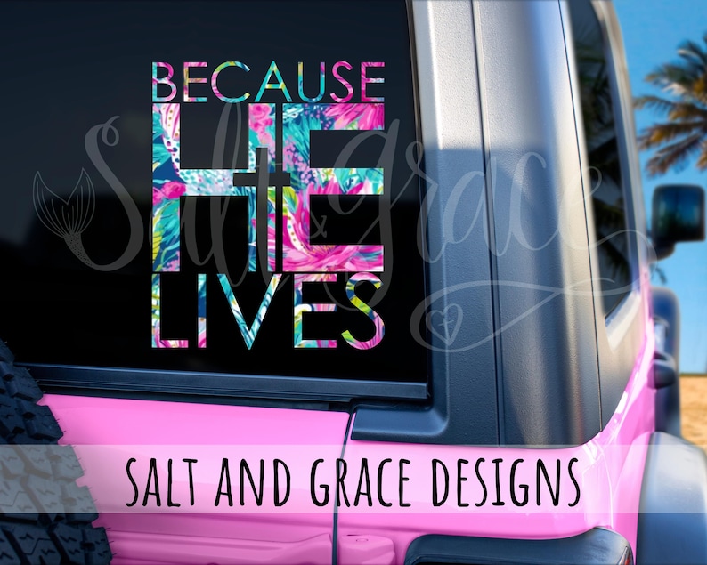 May include: A pink vehicle window decal with the words "BECAUSE HE LIVES" in a colorful floral pattern. The text "SALT AND GRACE DESIGNS" is below the main text. The decal is on a pink vehicle.