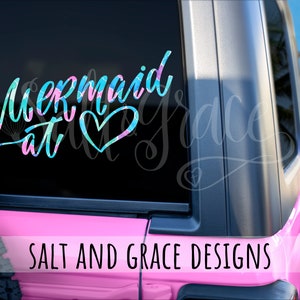 May include: A pink Jeep with a mermaid at heart decal on the rear window. The decal is in blue, green, and pink colours. The text "Salt and Grace Designs" is printed on the back of the Jeep.