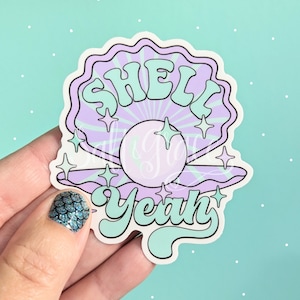 May include: A sticker with a purple seashell with a pearl inside and the text "Shell Yeah" in green letters. The sticker has a white background and is surrounded by small white dots.