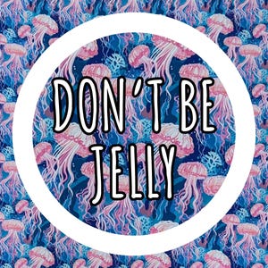 Op de afbeelding: Een levendig patroon met roze kwallen tegen een diepblauwe achtergrond. Het ontwerp bevat de tekst "DON'T BE JELLY" in een vetgedrukte, zwarte letter in een witte cirkel. Het thema is marien.