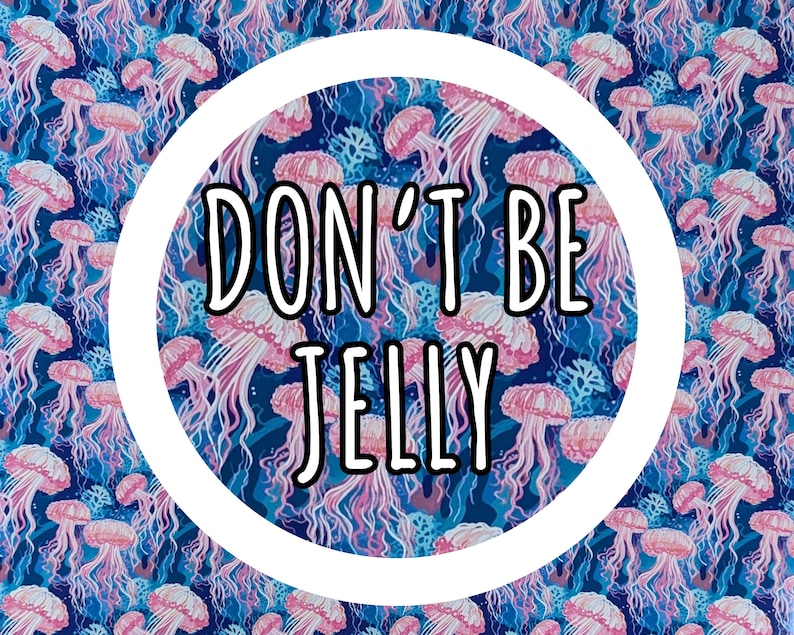 Op de afbeelding: Een levendig patroon met roze kwallen tegen een diepblauwe achtergrond. Het ontwerp bevat de tekst "DON'T BE JELLY" in een vetgedrukte, zwarte letter in een witte cirkel. Het thema is marien.