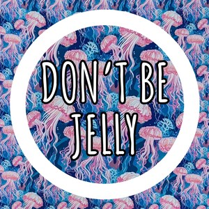 Może przedstawiać: Żywy wz&oacute;r z r&oacute;żowymi meduzami na ciemnoniebieskim tle. Projekt zawiera tekst "DON'T BE JELLY" w czarnym kolorze w białym okręgu. Og&oacute;lny motyw to życie morskie.