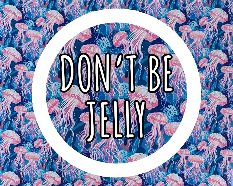Może przedstawiać: Żywy wz&oacute;r z r&oacute;żowymi meduzami na ciemnoniebieskim tle. Projekt zawiera tekst "DON'T BE JELLY" w czarnym kolorze w białym okręgu. Og&oacute;lny motyw to życie morskie.