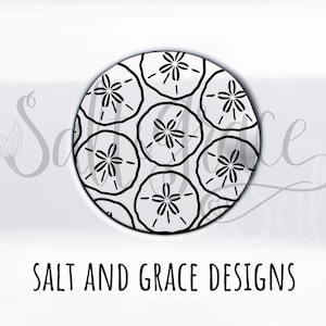 May include: A round, white coaster featuring a repeating pattern of black sand dollar designs. The text "SALT AND GRACE DESIGNS" is printed in black at the bottom of the coaster.