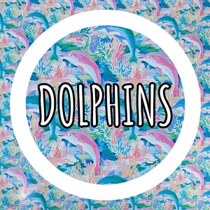 Op de afbeelding: Een kleurrijk patroon met dolfijnen in blauw en roze, omringd door koraal en waterplanten. Het woord "DOLPHINS" staat in een witte cirkel. Geschikt voor diverse toepassingen.