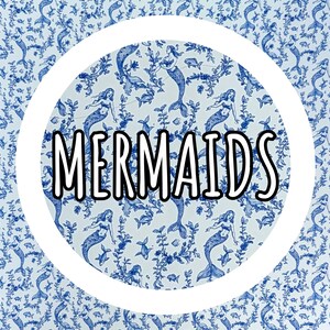 Op de afbeelding: Een wit cirkelvormig ontwerp met het woord "MERMAIDS" in zwarte letters met een witte omlijning, tegen een blauw en wit zeemeerminpatroon. Het patroon bevat zeemeerminnen, vissen en waterplanten.