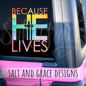 May include: A pink vehicle with a window decal that reads "BECAUSE HE LIVES" in colorful, watercolor-style lettering. A cross is incorporated into the design. The words "SALT AND GRACE DESIGNS" are printed at the bottom.