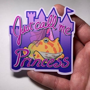 Puede incluir: Una pegatina morada y rosa con una rana de dibujos animados que lleva una corona y el texto "Just call me princess".