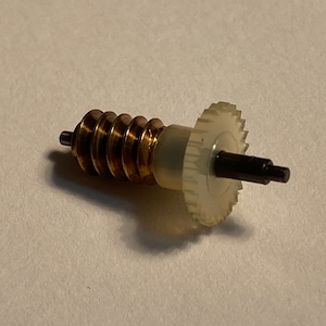 May include: A mechanical gear assembly featuring a brass worm gear and a white plastic spur gear. The gears are connected by a black shaft. The assembly is designed for mechanical applications.